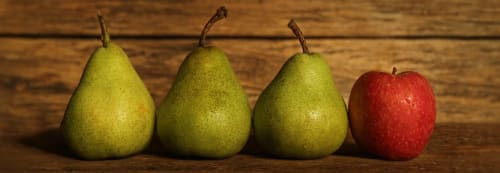 Tre gröna päron och ett rött äpple uppradade.