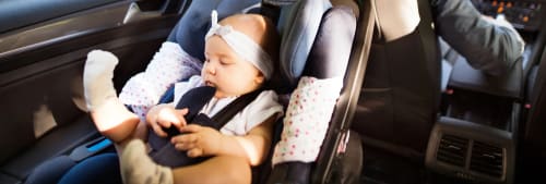 Baby som sitter i en bilbarnstol i baksätet på en bil. Skaffa barn ekonomi.