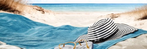 Bild på en handduk, solhatt och ett par tofflor på en sandstrand