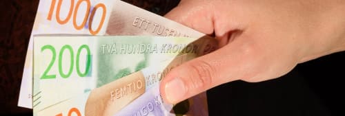 En hand med en 100 kr sedel och en 200 kr sedel