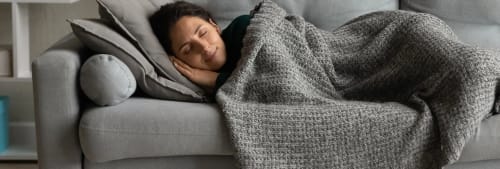 Bil på en kvinna som sover i soffan under en filt