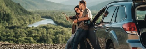 Ett par som stannat med bilen på utsiktsplats och står och tittar på en karta vid en bil.