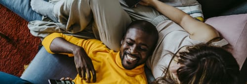 Kille skrattar i soffan med huvudet i flickvännens knä.