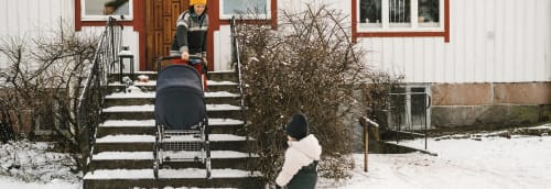 Kvinna som drar upp en barnvagn för en snötäckt trappa till ett hus.