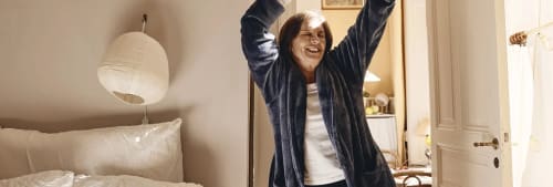 Jätteglad kvinna i morgonrock med händer ovanför huvudet.