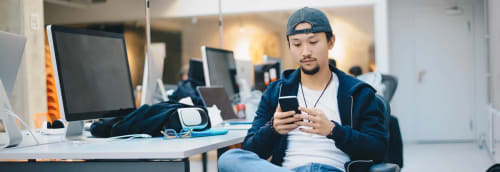 Ung cool kille sitter vid datorskärmar och tittar på mobilen.