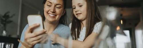 Mamma och dotter kollar på en mobil tillsammans.