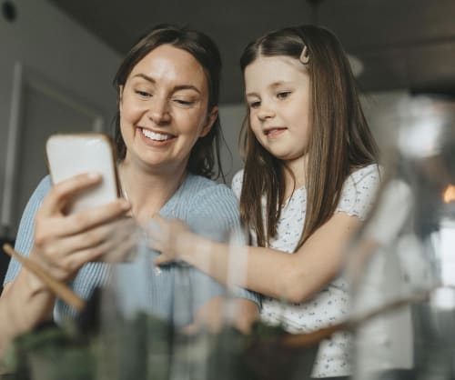 Mamma och dotter sitter och tittar på en mobiltelefon tillsammans.