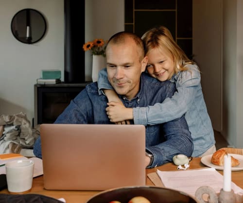 Pappa som sitter vid en dator och blir kramad av sin dotter.