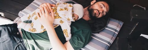 Pappa ligger i en säng med sin bebis på magen.