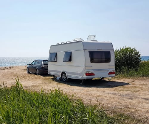 Bil med en husvagn som är parkerad vid havet. Låna till husvagn eller husbil hos ICA Banken.
