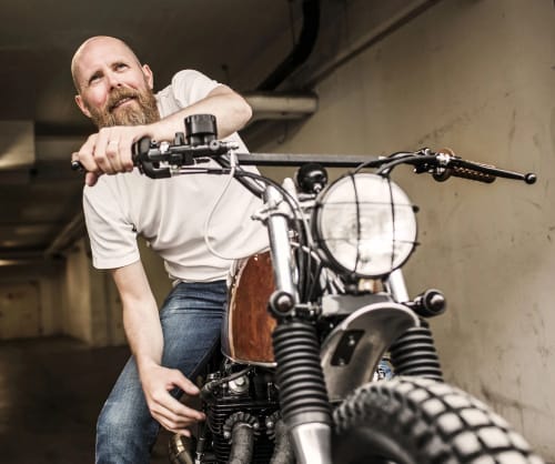 Man som sitter på en motorcykel i ett garage. Låna till motorcykel med ICA Bankens MC lån.