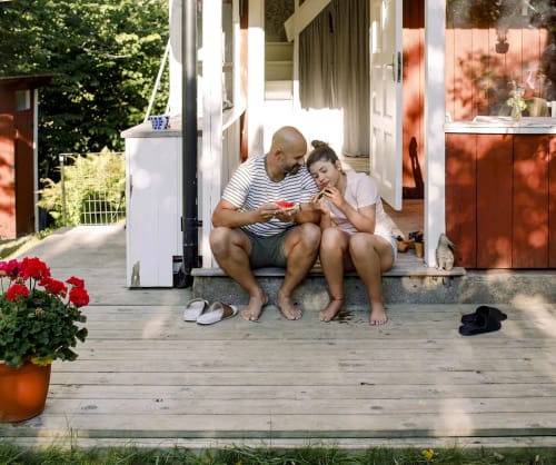 Pappa och dotter sitter på trappsteget till en sommarstuga. Låna till fritidshus med vårt fritidshuslån.