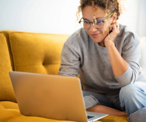 Kvinna som sitter i soffan med sin dator.