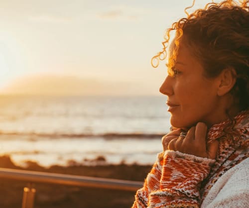 Kvinna som tittar mot solnedgången över havet.