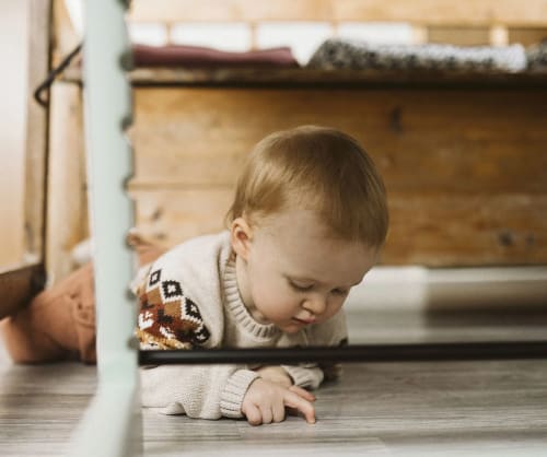 Bebis ligger under ett bord och pillar på golvet.