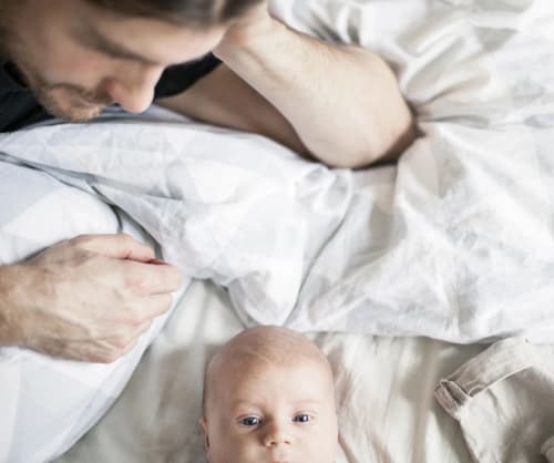 Pappa ligger i en säng och tittar på sin bebis.