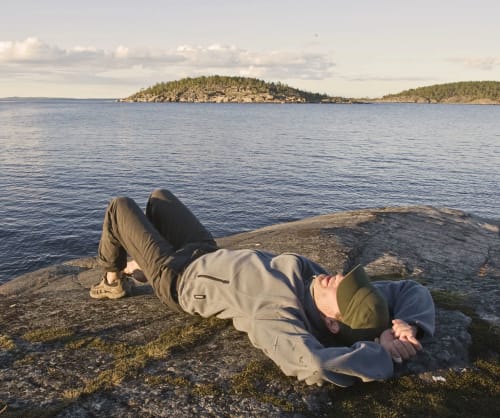 Man som ligger på en klipphäll vid havet och tittar mot himlen. Fondspara på ISK hos ICA Banken till dina drömmar.