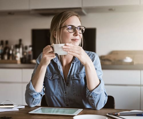 Kvinna tittar drömmande mot ett fönster. Spara i fonder till dina drömmar på ett depåkonto hos ICA Banken.