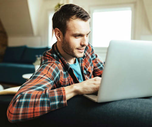 Man surfar på en dator i soffan. Hos ICA Banken kan du fondspara på ett ISK-konto.