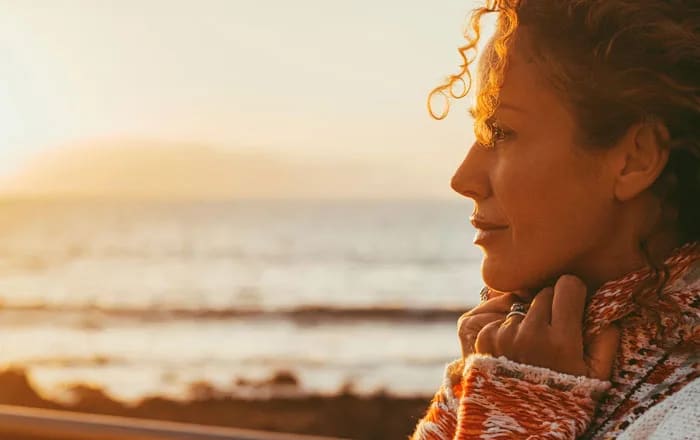 Kvinna drömmer sig bort och tittar mot solnedgången.