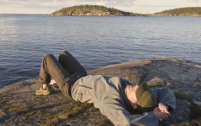 Kille som ligger och drömmer på en klippa vid havet.