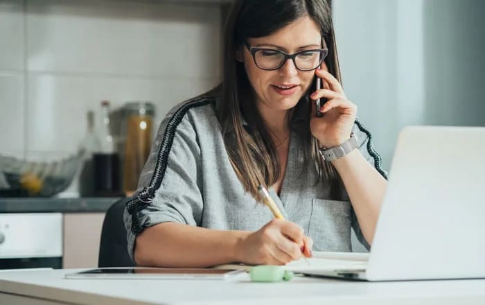 Kvinna framför en dator som talar i telefon. Boka möte om bolån.