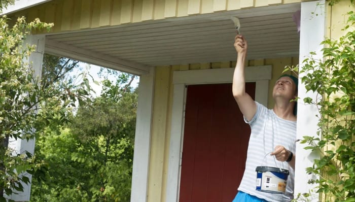 En man som står på en målar om sitt hus.