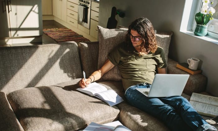 Man som sitter och pluggar i soffan hemma.