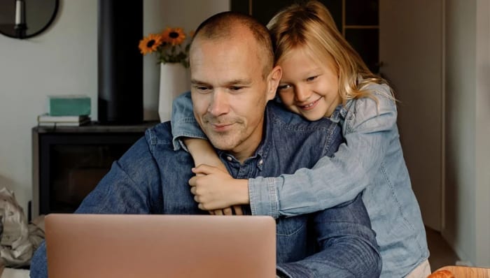 Dotter kramar pappa som sitter vid sin dator.