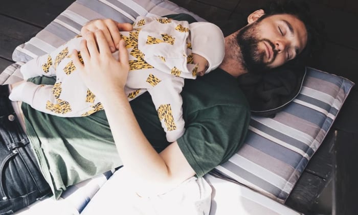 Sovande pappa som ligger på en madress med en sovande bebis på magen.