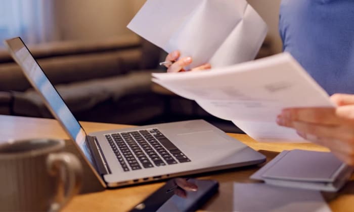 Man som sitter vid en dator med papper i sin händer.