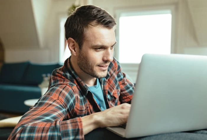Kille som halvligger i en soffa med en laptop framför sig.