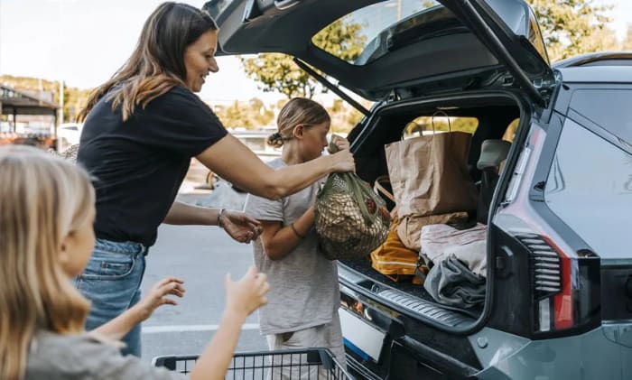 Mamma och barn som packar in kassar i bakluckan på en bil.