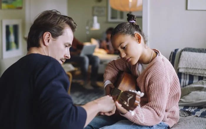 Pappar lär dotter att spela gitarr.