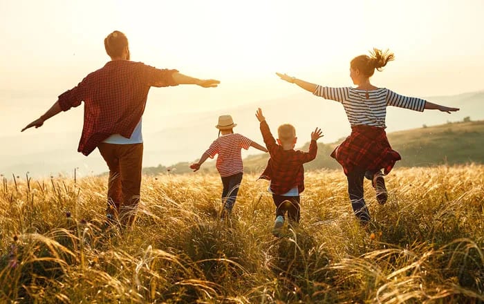 Familj med pappa, mamma coh två barn som går över ett fält.