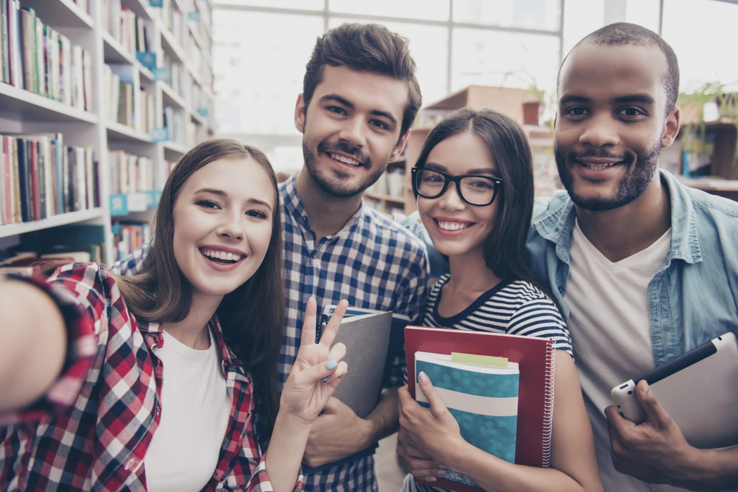 Fyra studenter, två tjejer och två killar, tar en bild i bibliotek. Alla ler.