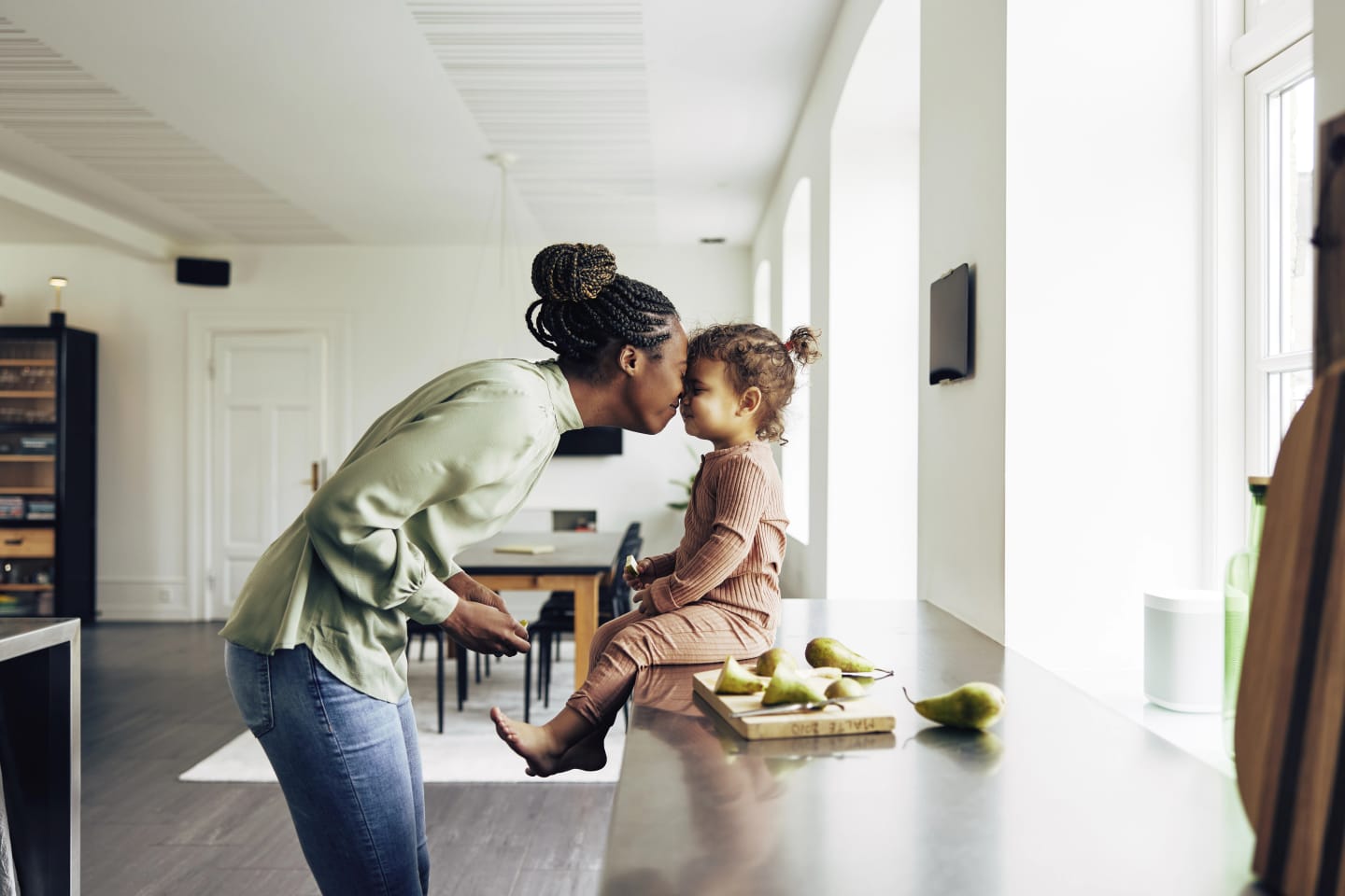 Mamma och dotter står i köket och trycker näsorna mot varandra och ler. Barnet sitter på köksbänken.