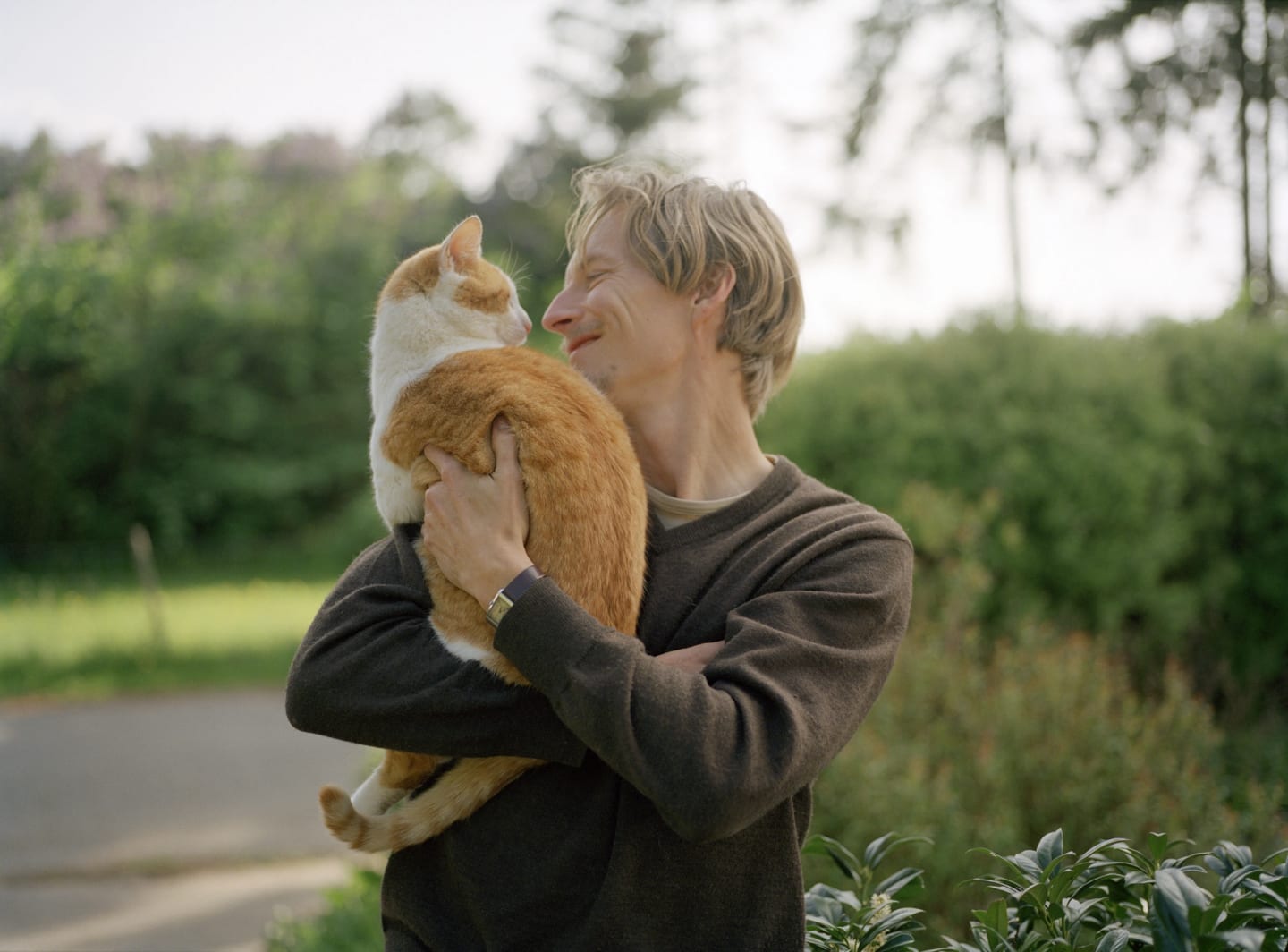 Man står utomhus och håller i en orange katt i famnen och ler.