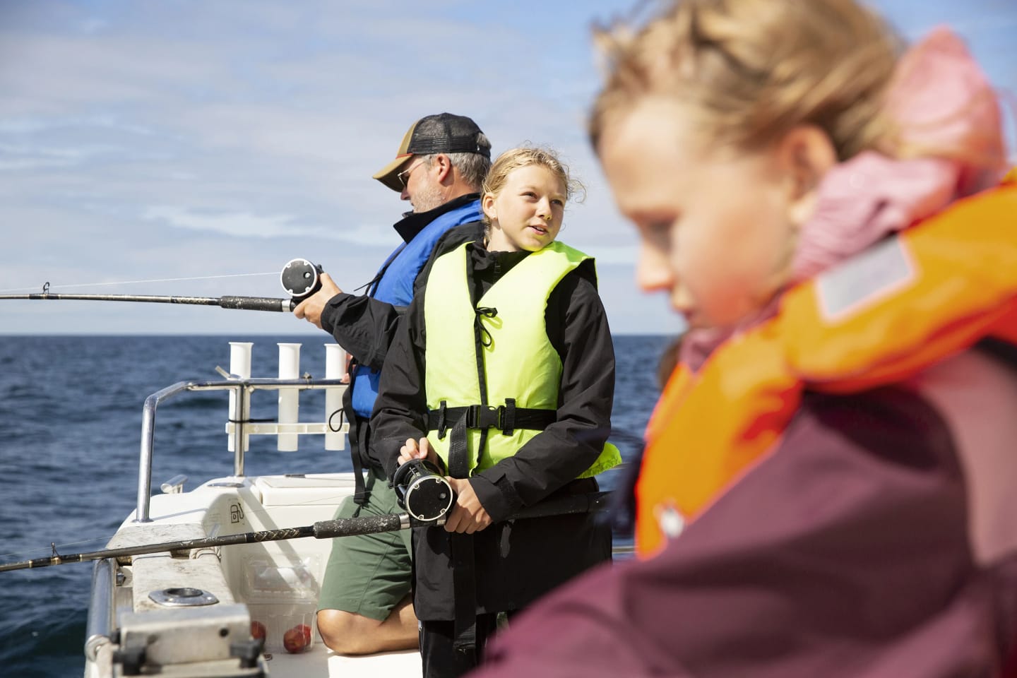 En pappa och två barn är ute på sjön med sin motorbåt ock fiskar.