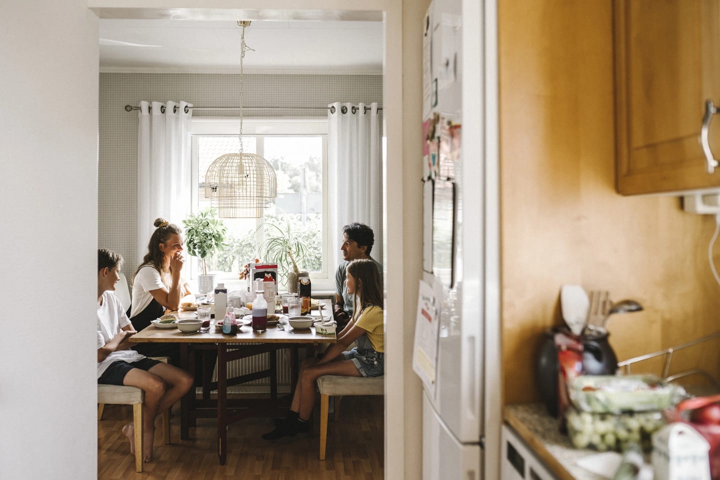 Bild tagen från köket där man ser familj på två vuxna och två barn äta frukost tillsammans.