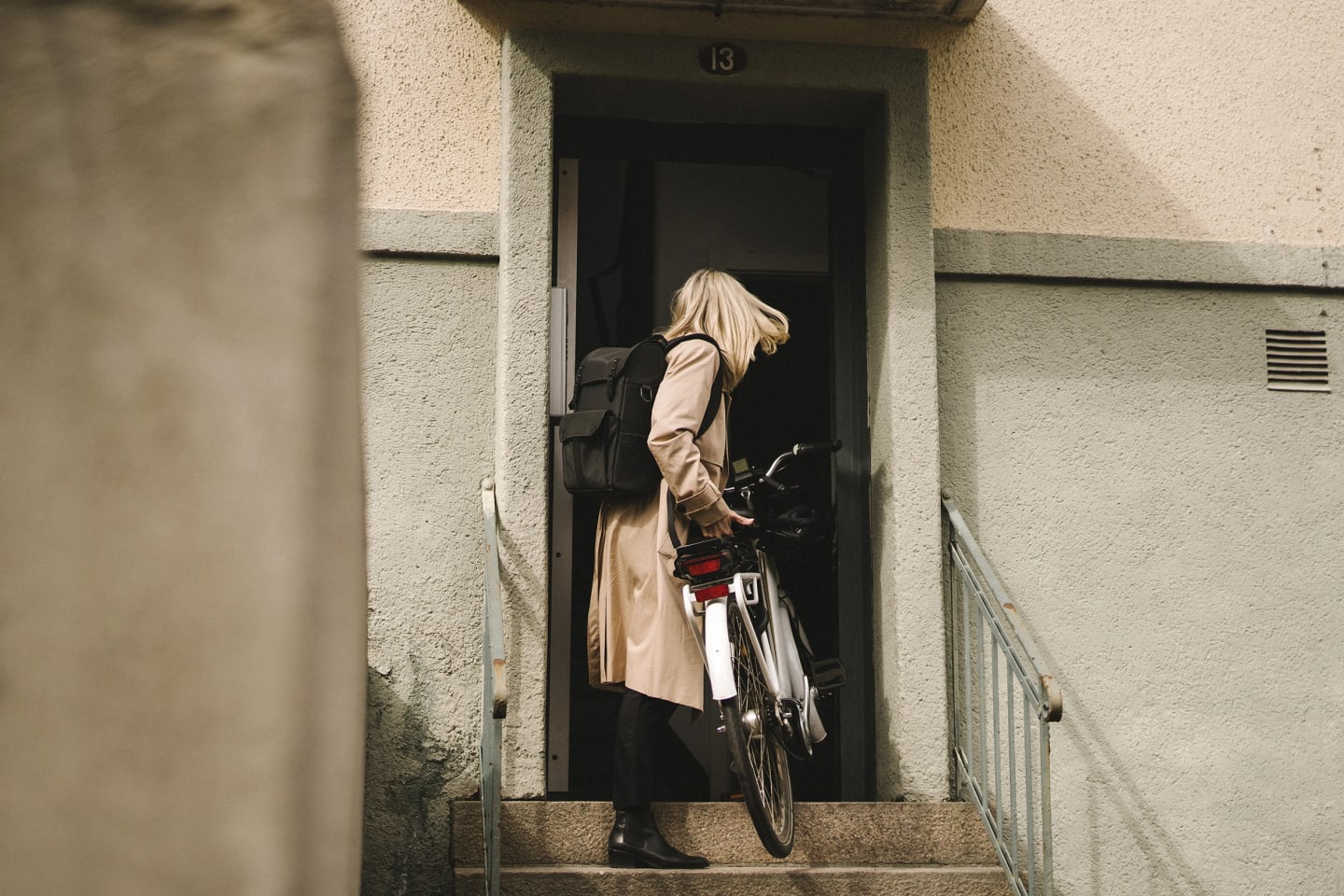 En kvinna står vid trappuppgång med cykel i handen på väg in.