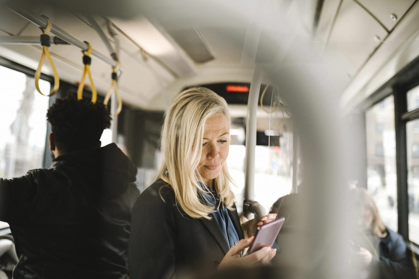 Kvinna står på buss och tittar i telefonen