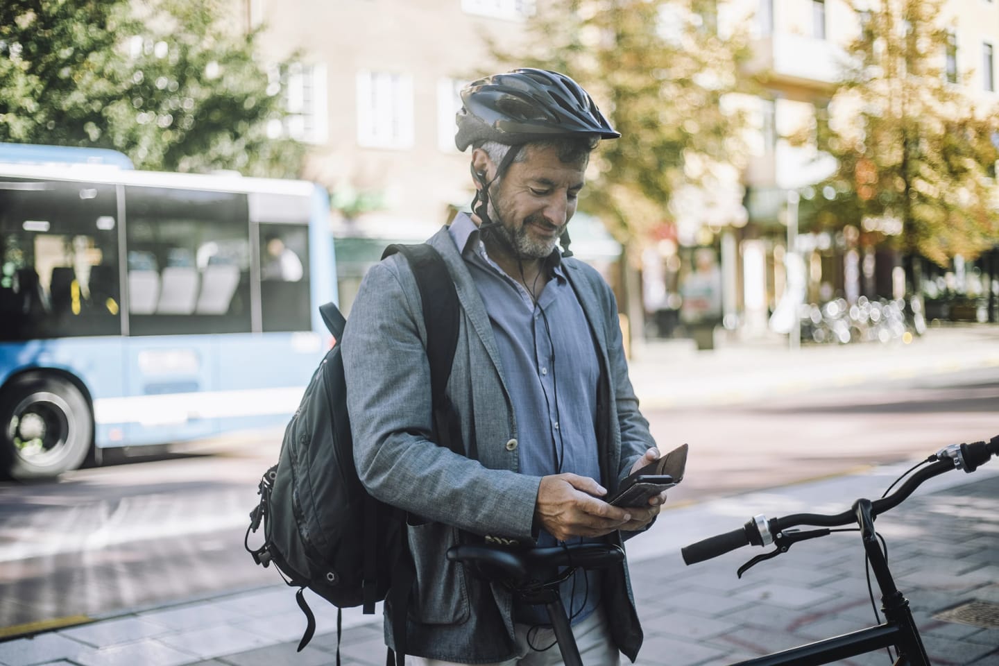 En medelålders man står med cykeln parkerad bredvid en väg och tittar ner i telefonen.