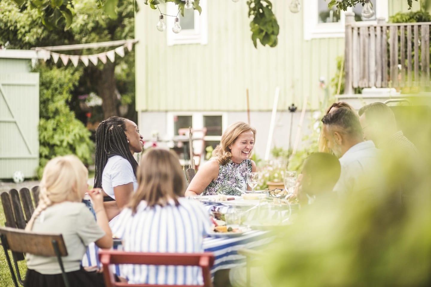 Personer sitter utomhus i trädgården vid matbordet och skrattar