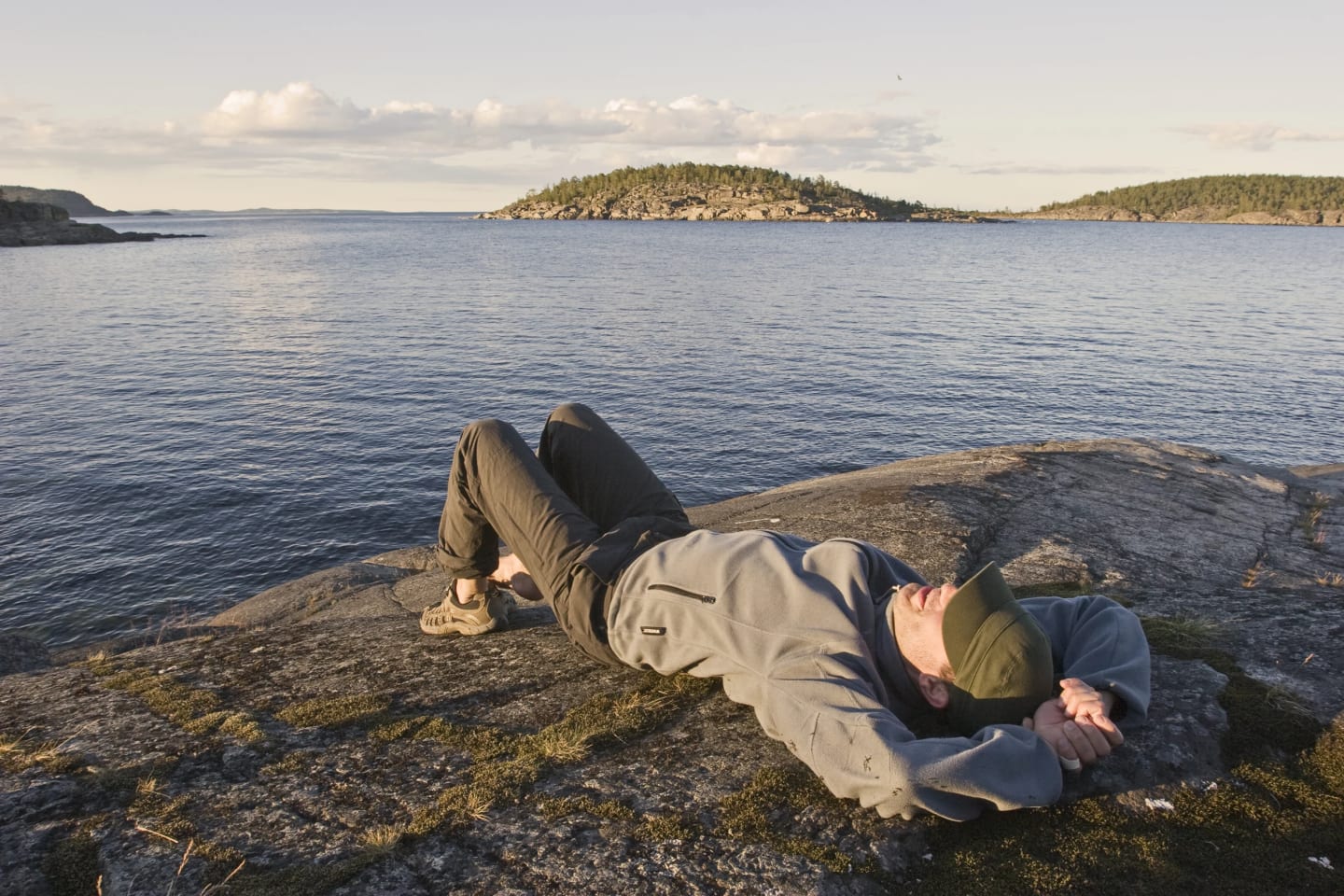 En man ligger på en klippa vid havet och vilar.