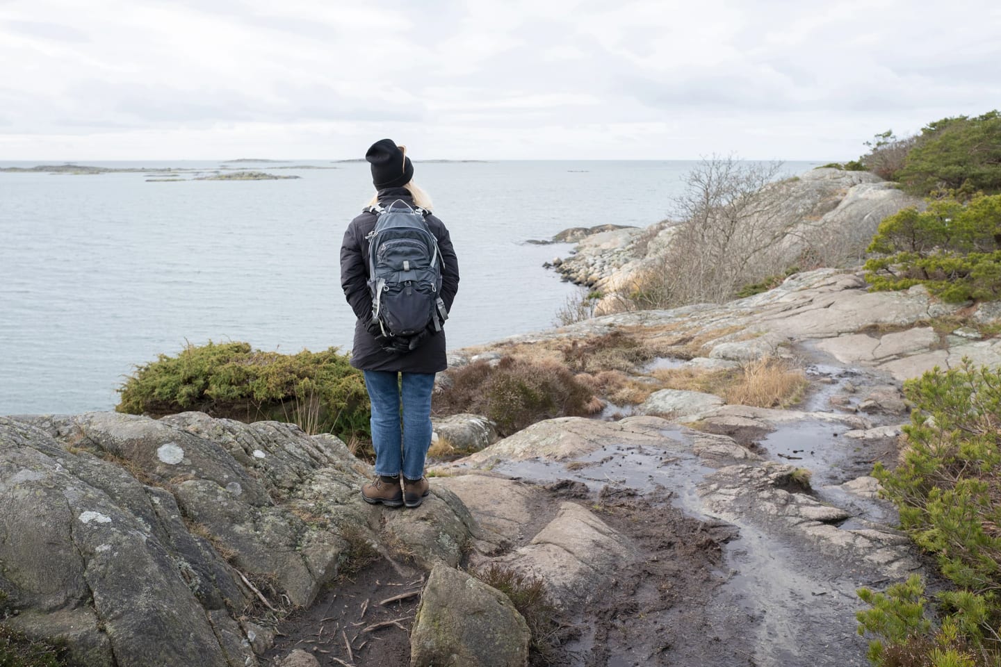 Bild tagen bakifrån där en kvinna står på ett berg och tittar ut på havet.