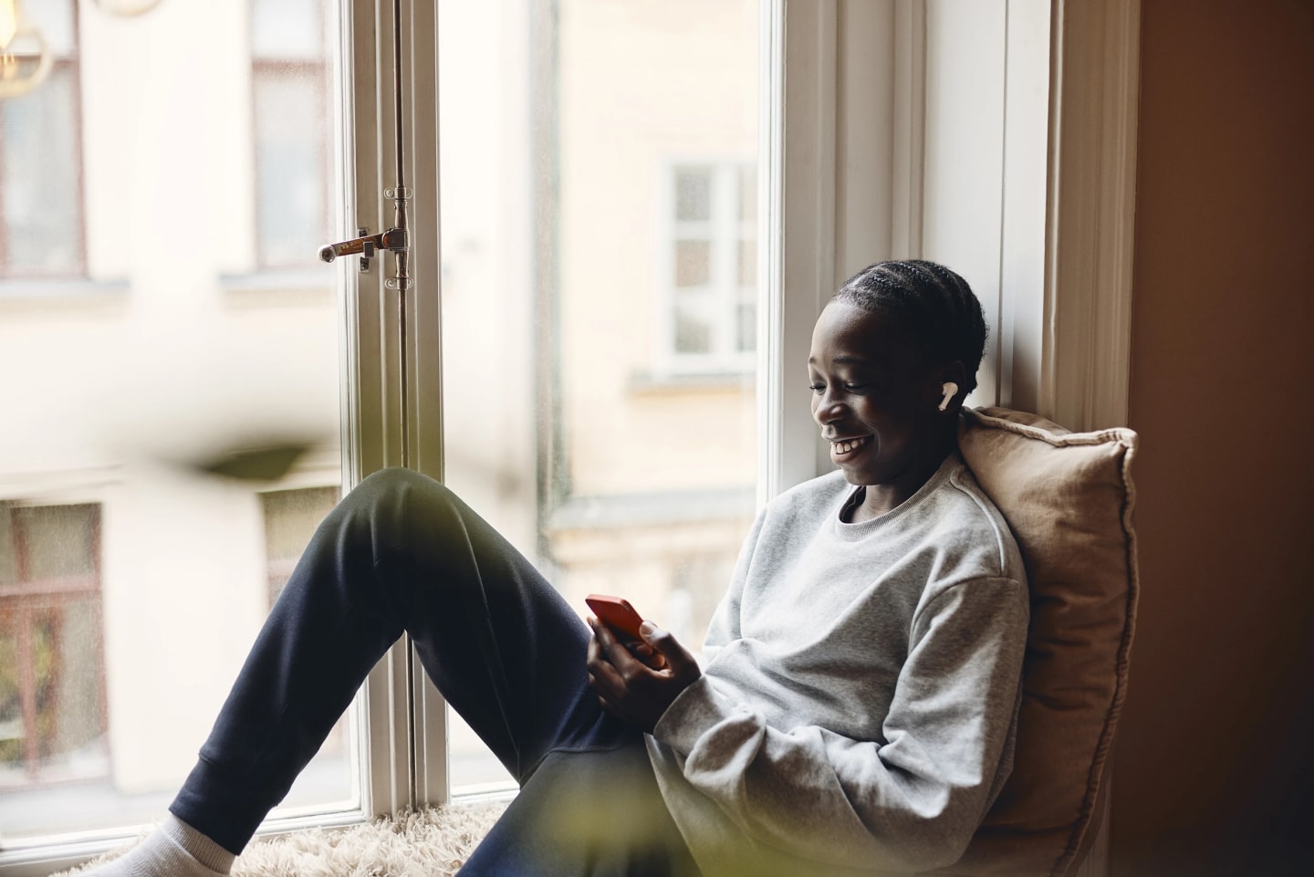 Ungdom sitter i fönstret och tittar på telefonen och ler