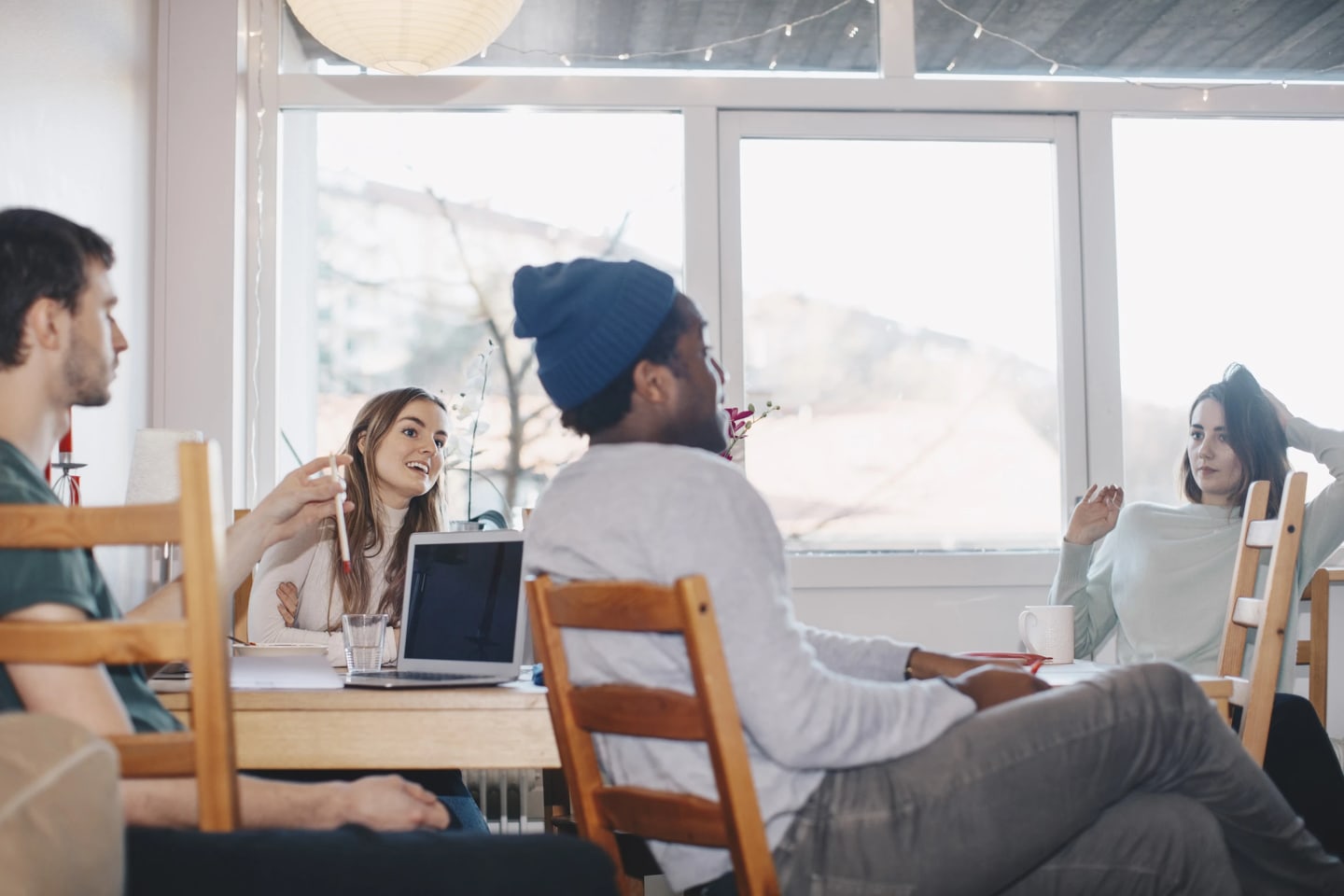 Fyra studenter sitter vid ett matbord med datorer och diskuterar något.