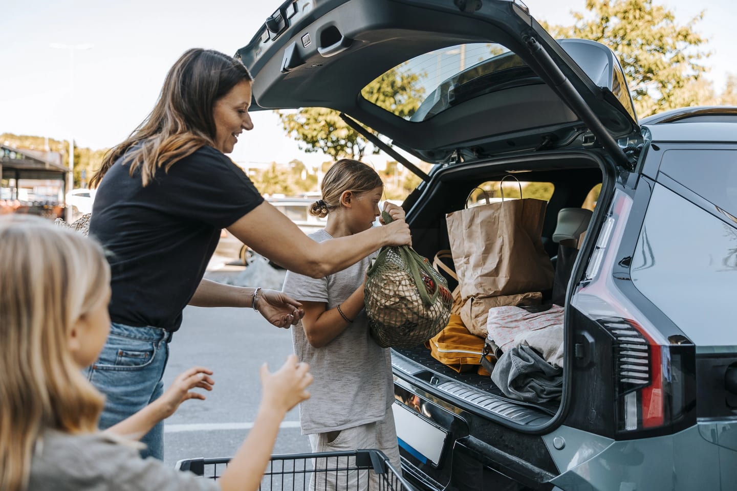 En mamma och hennes två barn lägger in matvaror i bakluckan på sin bil.